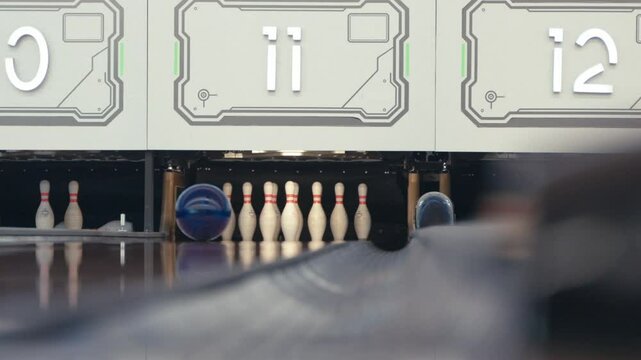 Asian person in casual outfit rolls a bowling ball smoothly on the lane toward the pins, captured indoors with clear background, showing focus, motion, and game preparation
