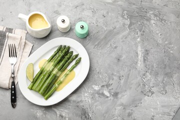 Tasty cooked asparagus served with sauce and lime on grey textured table, flat lay. Space for text
