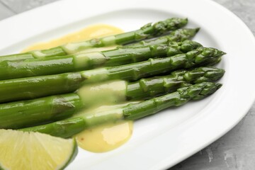 Tasty cooked asparagus served with sauce and lime on grey textured table, closeup