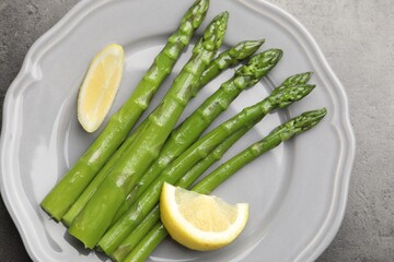 Tasty cooked asparagus served with lemon on grey table, top view