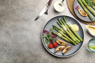 Tasty cooked asparagus served with baked potatoes, tomatoes and sauce on grey table, flat lay. Space for text