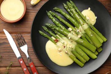 Tasty cooked asparagus served with sauce on wooden table, flat lay