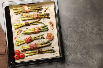 Tasty cooked asparagus with bacon, tomatoes and spices in baking tray on grey table, top view....