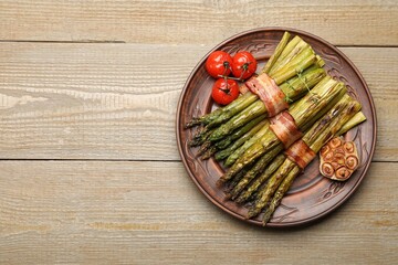 Tasty cooked asparagus served with bacon and spices on wooden table, top view. Space for text