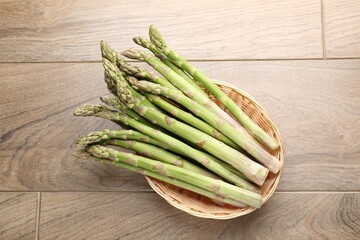 Fresh raw asparagus spears in wicker basket on wooden table, top view