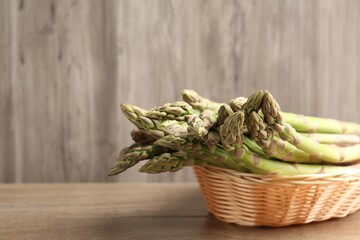 Fresh raw asparagus spears in wicker basket on wooden table, closeup. Space for text