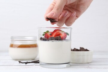 Woman adding chocolate pieces to tasty panna cotta at white wooden table, closeup