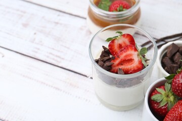 Tasty panna cotta with chocolate, strawberries, vanilla pods and caramel on white wooden table, closeup. Space for text
