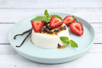 Tasty panna cotta with chocolate, strawberries, mint, caramel and vanilla pods on white wooden table, closeup