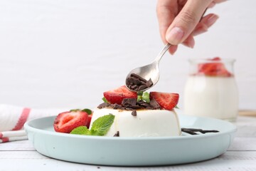 Woman adding chocolate pieces to tasty panna cotta at white wooden table, closeup