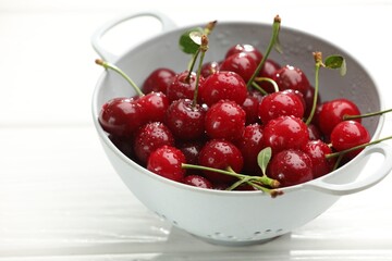 Fresh wet cherries in colander on white wooden table, closeup