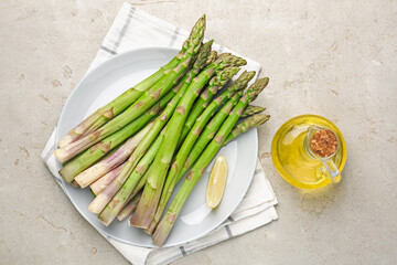 Fresh raw asparagus, oil and lemon on light grey table, flat lay