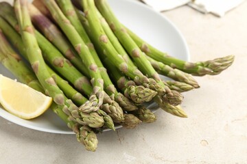Fresh raw asparagus and lemon on light grey table, closeup