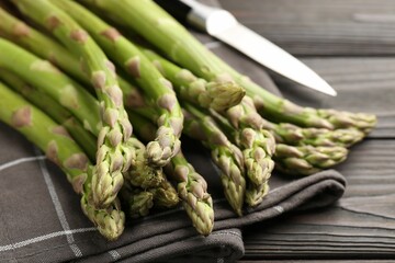 Fresh raw asparagus and knife on black wooden table, closeup