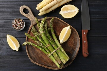 Different raw asparagus spears, spices and knife on dark wooden table, flat lay