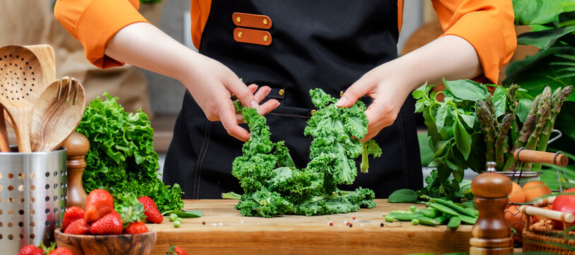 Chef woman prepares fresh kale and other vegetables in a vibrant kitchen, showcasing her healthy, vegan cooking style and passion for food.