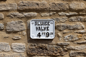 Old metal Sluice Valve sign on stone wall