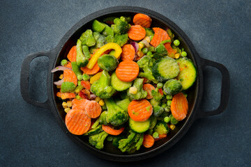 Frozen vegetables in a cast iron round frying pan. Cooking vegetable dishes.