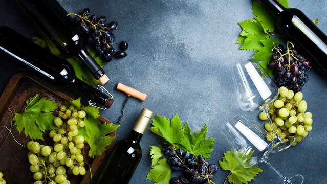 Composition of wine bottles, glasses, grapes and grape leaves on a stone table. Top view. Free space for text.