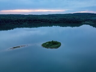 Smooth lake surface at dusk with islands on the water, aerial drone view.