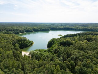 Aerial panoramic view of a clear-water lake at sunrise, surrounded by forest. Treetops are...