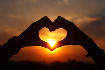 silhouette of hands making a heart shape. two hands making a heart shape. a close up view of a sunset with the sun shining through