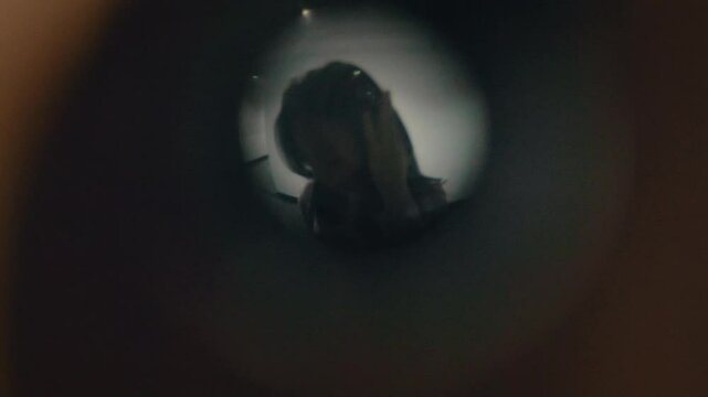 Asian woman in casual outfit looks through a door peephole indoors with clear background, showing cautious gesture, awareness, security action, and natural everyday lifestyle moment