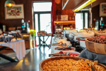 Hotel breakfast buffet with various cereals, fruits, cheeses, and cold cuts in bowls and trays. Elegant setup with modern interior, self-service arrangement, and warm lighting
