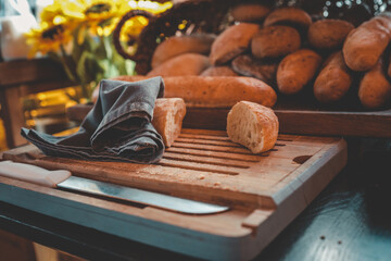 Fresh baguettes and bread rolls on wooden cutting board with knife and napkin. Rustic breakfast or...