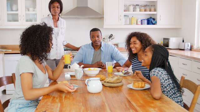 Family With Teenage Children Eating Breakfast Around Table In Kitchen