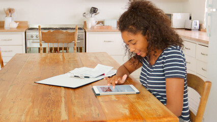Teenage Girl With Digital Tablet Revising For Exam Sitting At Table At Home