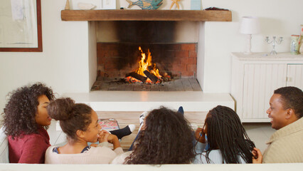 Rear View Of Family Sitting On Sofa In Lounge Next To Open Fire