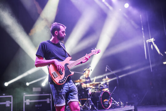 Bass guitarist and drummer performing live on stage with bright spotlights