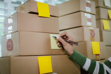 An Asian female entrepreneur works on her laptop to manage the logistics of her e-commerce business, organizing parcels, processing orders, and managing online sales and deliveries from her home offic