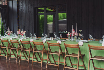 Elegant wedding reception setup with green tablecloth and floral decorations at outdoor venue,...