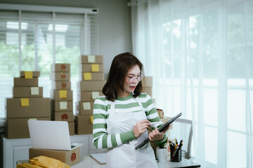 A young woman entrepreneur manages her online business from home, surrounded by parcel boxes, using a laptop, calculator, and notepad to handle shipping and inventory.