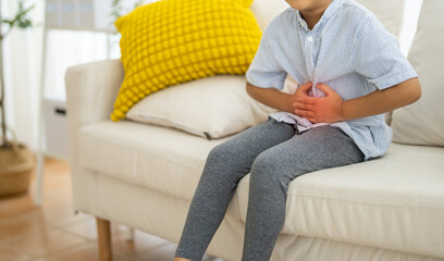 Portrait of sick unhappy little child asian boy touching belly stomach with suffering from stomach...