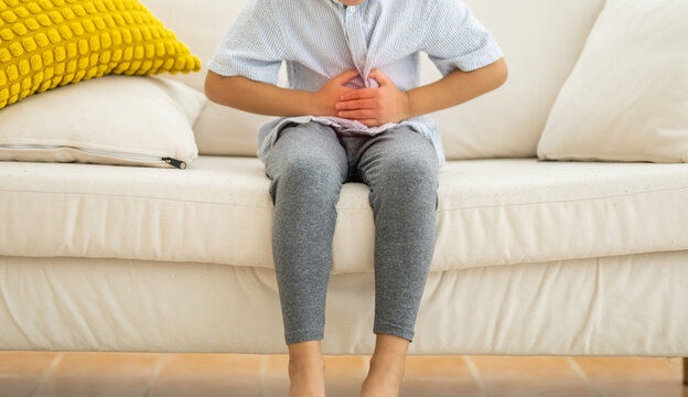 Portrait of sick unhappy little child asian boy touching belly stomach with suffering from stomach ache pain, gastritis, gastroenteritis, food poisoning, diarrhea, intestinal inflammation at home