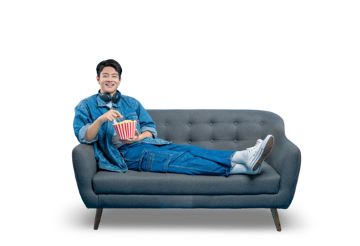 PNG,A relaxed young man lounging on a sofa reaches for popcorn while watching a movie or TV show.
