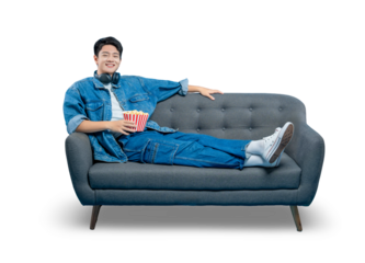 PNG,A smiling young man in a denim jacket relaxes on a sofa with a bucket of popcorn, enjoying a day of leisure at home.
