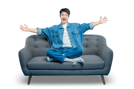 An excited young man sits on a sofa with his arms open wide in a joyful and welcoming gesture.PNG