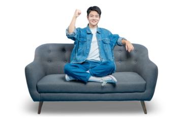 A young man on a sofa celebrates with a fist pump gesture, cheering for his favorite team or a movie hero.PNG