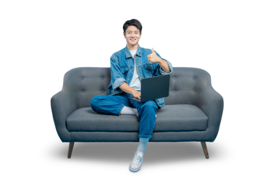 A smiling young man sits on a sofa with a laptop and gives a thumbs-up, showing approval for online content or services.PNG