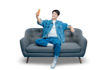 A cheerful young man in casual attire sits on a sofa and takes a selfie with his smartphone, perfect for social media concepts.PNG