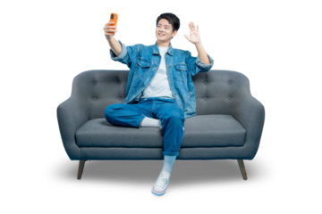 A happy young man sits on a sofa while taking a selfie or having a video call, waving hello to the camera.PNG