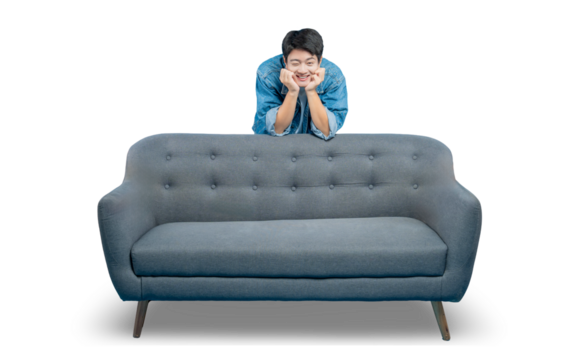 A young man with a cute, winking expression rests his chin on his hands while peeking over an empty sofa.PNG