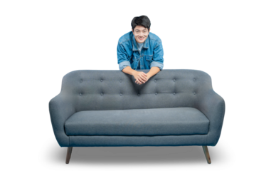 A friendly young Asian man leans on the back of a sofa, peeking over with a welcoming smile.PNG