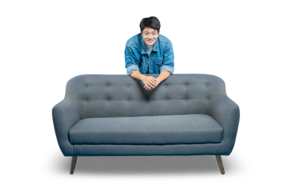 A friendly young Asian man leans on the back of a sofa, peeking over with a welcoming smile.PNG