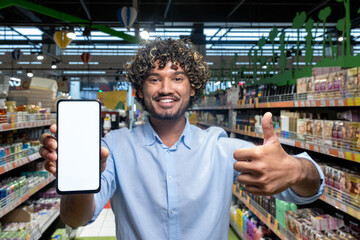 A man holding a phone with a blank screen in a supermarket, giving a thumbs-up, promoting online...