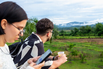 Man and woman at sunset in mountains. Young adults are engaged with their smartphones while...